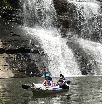 Two people in an inflatable kayak in front of waterfall