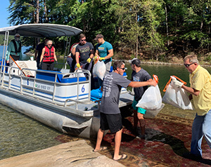 volunteers on boat handing off trash bags to volunteers on land