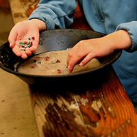 Child's hand holding gemstones as they take them out of a pan.