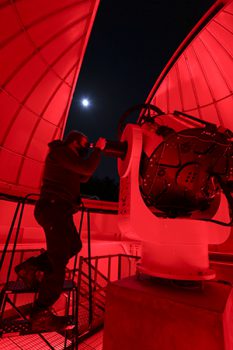 Dramatic red and black photo of a UNG student working with a telescope