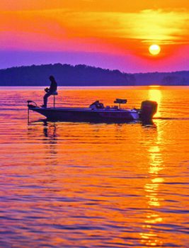 Fishing from a powerboat at sunset with purple orange reflections and sky.