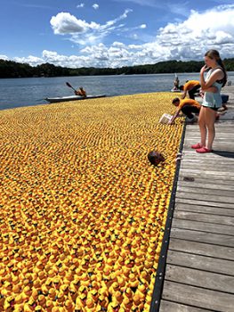 Man in water with only head showing among all the floating rubber ducks. 