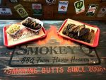Two trays of food on wooden table with Smokey Q logo and mac and cheese, ribs and bbq. 