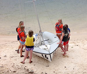 Students on land with sailboat getting ready to launch boat into lake.
