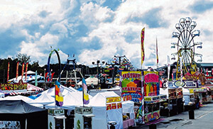 Booths lining the street with a ferris wheel in the background at the Cumming Country Fair and Festival.
