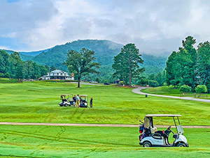 Golfers ridinding in golf carts on beautiful greens with mountain in background.