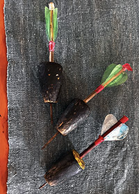 3 competition darts from Bhutan laying on a gray cloth. The wings are colorful green, blue, red. -