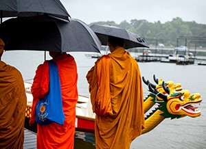 Monks in colorful robes, holding umbrellas, with backs to viewer, bless the dragon boats before racing.