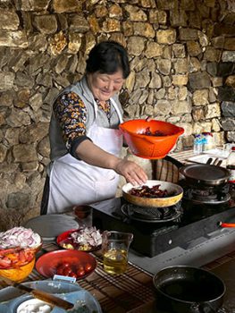 Bhutanese women in front of open stovetop area preparing food.