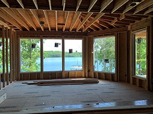 View from inside a remodel with raw floor and wood rafters exposed. New large windows with view of the lake.Inside 