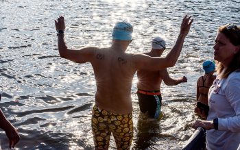 View of backs of three swimmers as they enter Lake Lanier for Swim Across America event