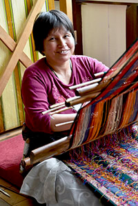 A Bhutanese woman sitting on the floor working a hand loom.