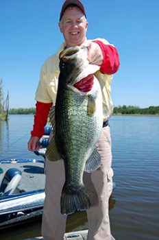 A fisherman holding his 11-pound bass with boat and water in the background.