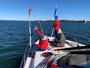 3 people dressed in winter clothing on front of boat on Lake Lanier during the Hot Ruddered Bum Sailing regatta.