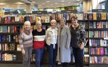 Five women, members of the Buford Lanier Womans Club book club stand in front of books at a local bookstore.