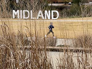 Runner on sidewalk in front of the Midland letters sign.