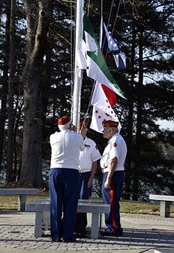 Three Color Guard members in uniform raising flags.