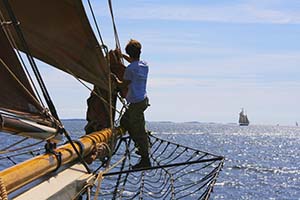 Young sailor standing on netting on side of ship to help raise the sail.
