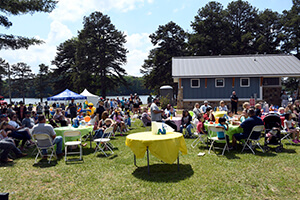 Grassy lawn by Lake Lanier with tables and people seated at the Boys and Girls Club of Lanier's Duck Derby.