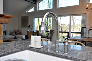 View of open concept kitchen with faucet large in front of view of many large windows.