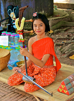A young Thai girl sitting on floor in a bright orange outfit holding a musical instrument.