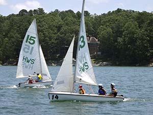 Students aboard two white sailboats. Sails are white with blue