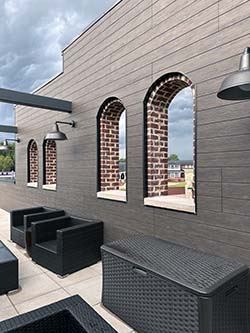 On rooftop, a wall with arched, open windows shows city in background. 
