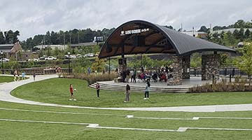 Wide view of Cumming City Center pavilion and stage with grassy terraced lawn and people of all ages about.