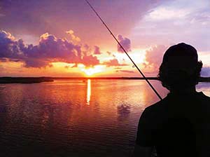 Silhouette of a boy fishing against an orange sunset.