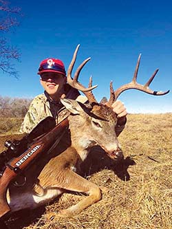 Young boy wearing a cap with a buck he shot.