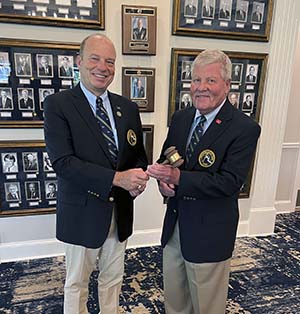 Both men dressed in navy blazers standing inside in front of other photos - Bret Benninghoff passing gavel to Steve Simpson.