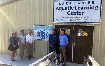 3 people standing in front of door and sign of the Lake Lanier Aquatic Learning Center.