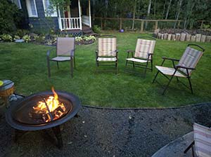Lawn chairs on green grass around a lit fire pit.