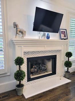 A new fireplace with white mantel, white walls and TV mounted over fireplace.