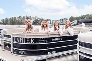 4 real esate team members sitting on front of a pontoon boat with trees and Lake Lanier in the background.