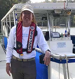 Captain John McCalpin standing by boat with cap and lifejacket on