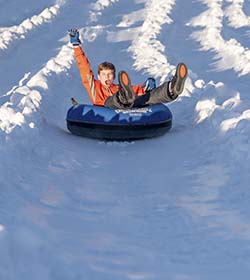 A young boy dressed in orange, laid back in a black snow tube sliding down Blizzard Mountain.