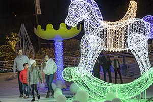 A family dressed in winter clothing looking up at large rocking horse in lights. 