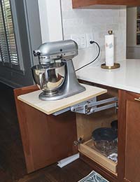 A stand mixer on a shelf that comes from inside a cabinet and can retract into cabinet when not in use.