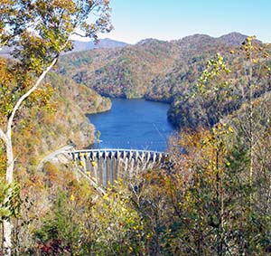 A view of the dam and lake surrounded by trees that show the last of the fall colors. 