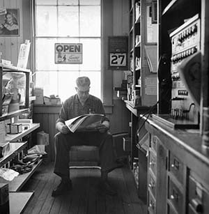 A copy of a black and white photo of a man sitting in a chair in front of a window in the McKenzie Store. 