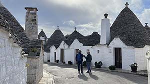 A couple of people walk down the street with the small, connected, white trulli homes on either side.