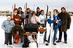 Group of people in coats with skis, a BBQ grill, and wreath all posing for photo.