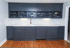 A newly installed wet bar painted in blue gray with silver hardware. Cabinets going to the ceiling on top, counter space with white backsplash, then cabinets on bottom.
