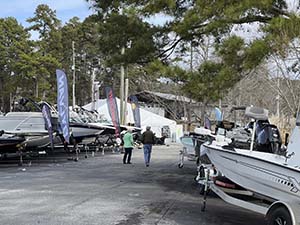 View of the backs of people as they walk on the road through the boat show, with boats on either side of them.