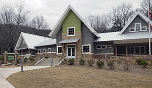 The front view of the new Visitor Center at Amicalola Park. It has a wide sidewalk leading to the front door of a stacked stone and green and gray board-and-batton building. 