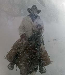A color photo that looks like a black and white photo of a man in a cowboy hat riding a horse through the snow in Blairsville, GA during the blizzard of 1993. 