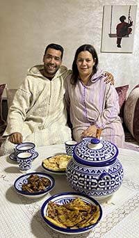 A couple from Fez sitting close together in front of the dinner table with blue and white dishes and traditional Moroccan food. 