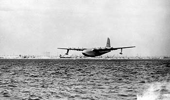 A black and white photo showing the Spruce Goose plane in flight. 