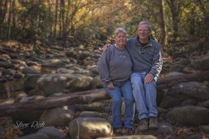 Ted and Dora McGee sitting close together on rocks in a stream. 